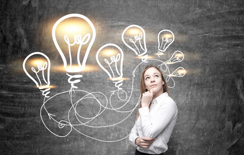 A woman stands in front of a chalkboard with drawings of illuminated light bulbs.